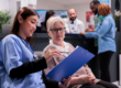 Healthcare professional discussing a patient safety document with an older woman in a busy clinical setting