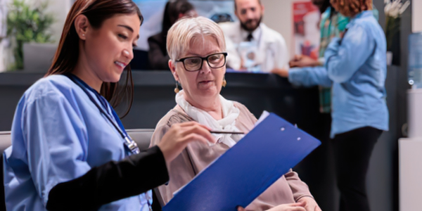 Healthcare professional discussing a patient safety document with an older woman in a busy clinical setting